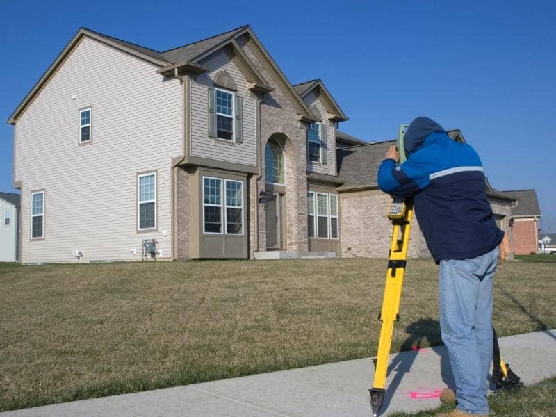 Surveyor performing a residential land survey at a suburban home to verify property boundaries